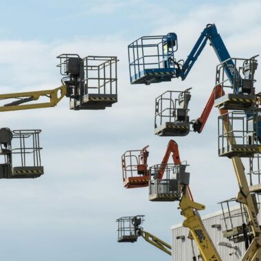A collection of colorful boom lifts reaching toward a clear blue sky, showcasing industrial machinery.