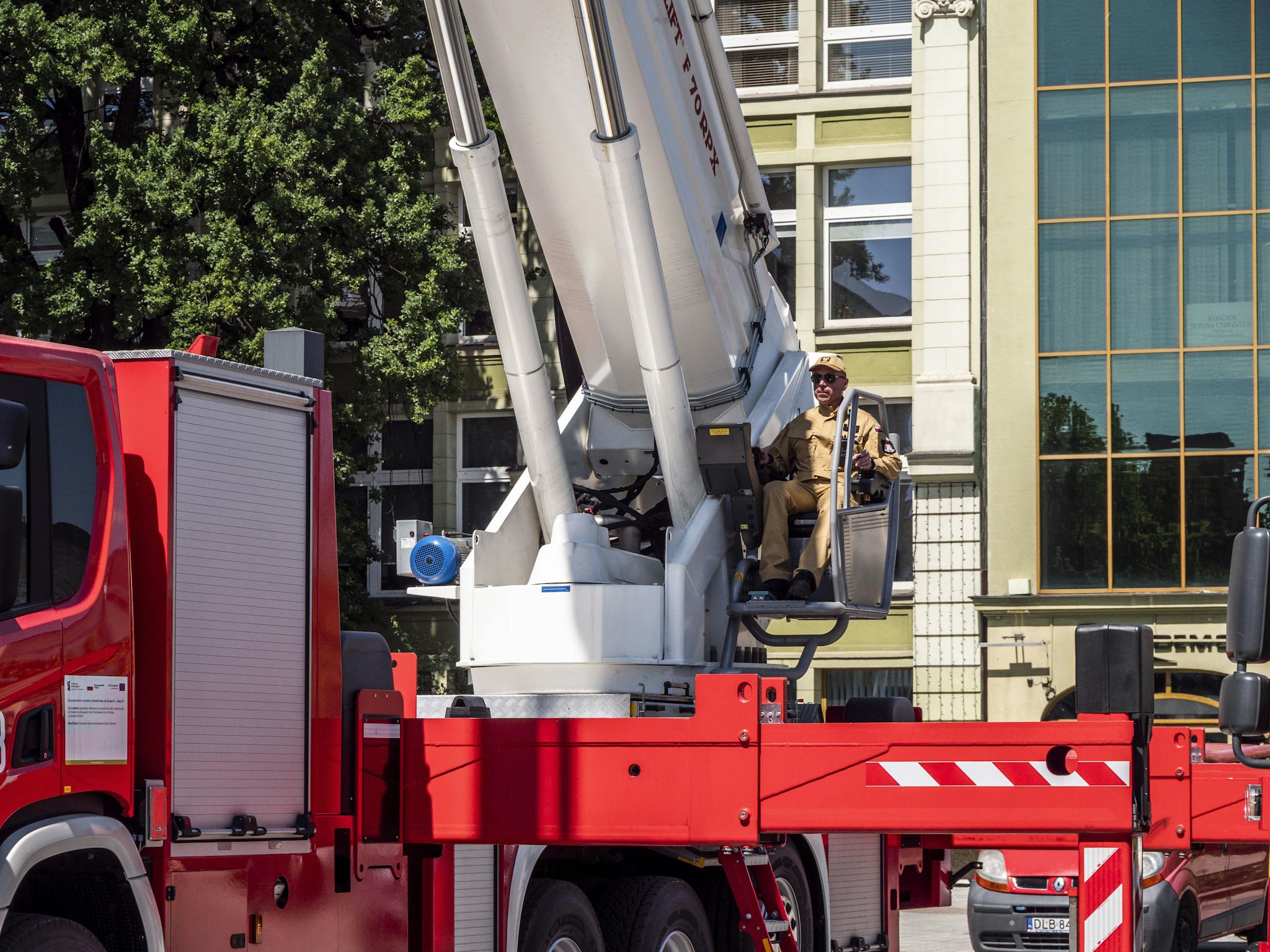 A construction worker operates a hydraulic lift on a red truck in an urban setting.