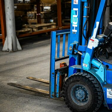 Blue forklift inside an industrial warehouse, parked near shelves with various items.