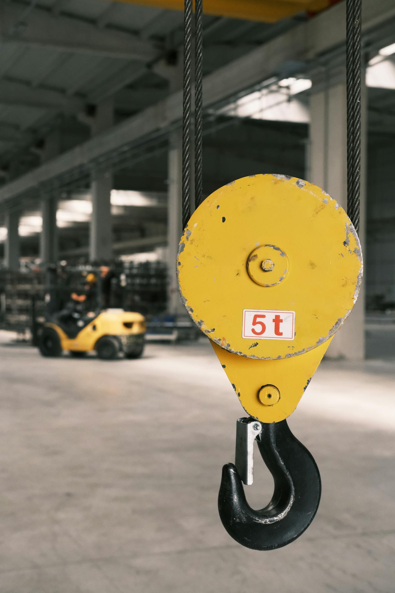 Closeup of a yellow industrial hook in a spacious factory with a focused background.