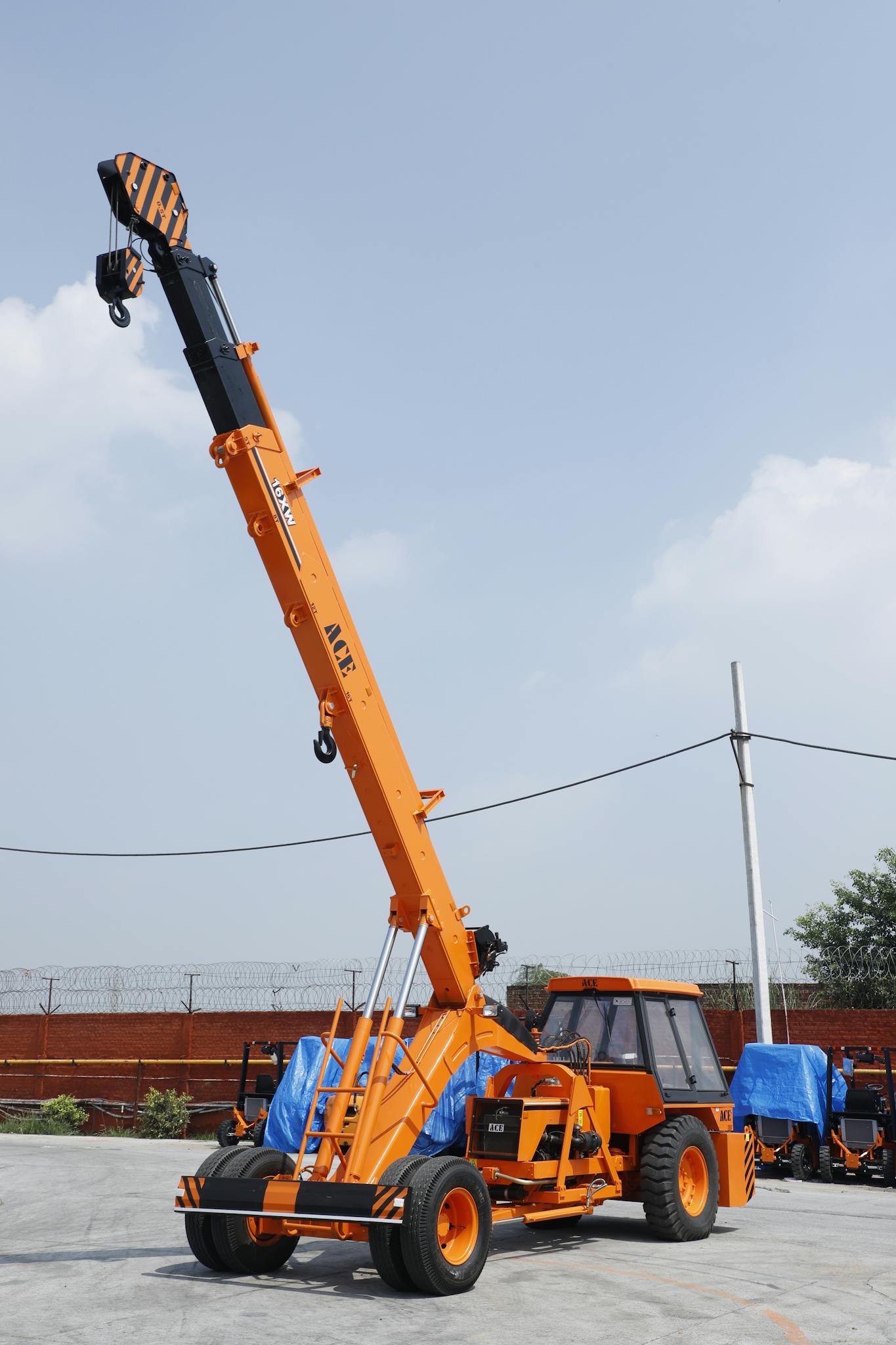 Orange ACE mobile crane in use at an outdoor construction site in Faridabad, India.