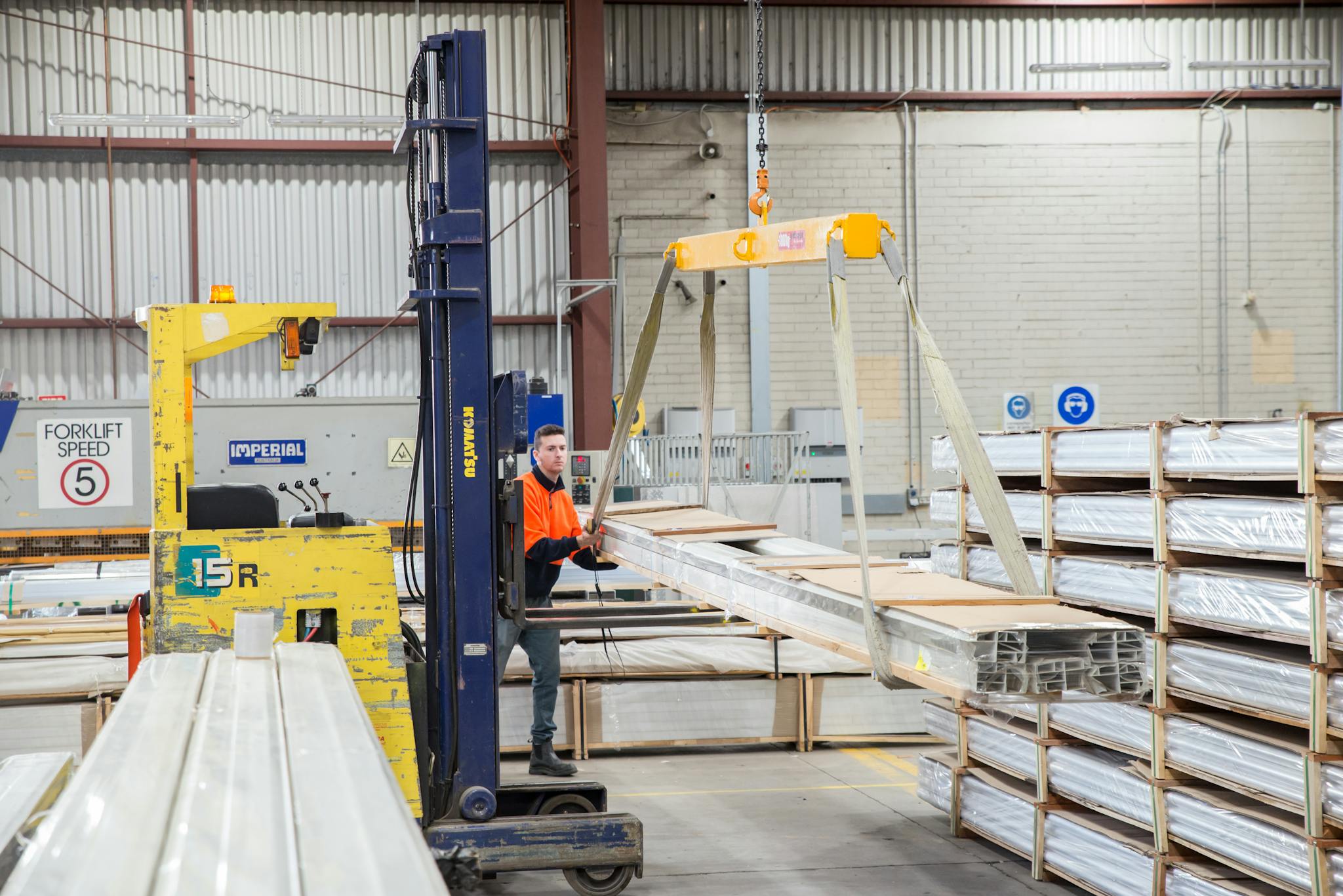 Warehouse scene with worker maneuvering forklift and crane system.
